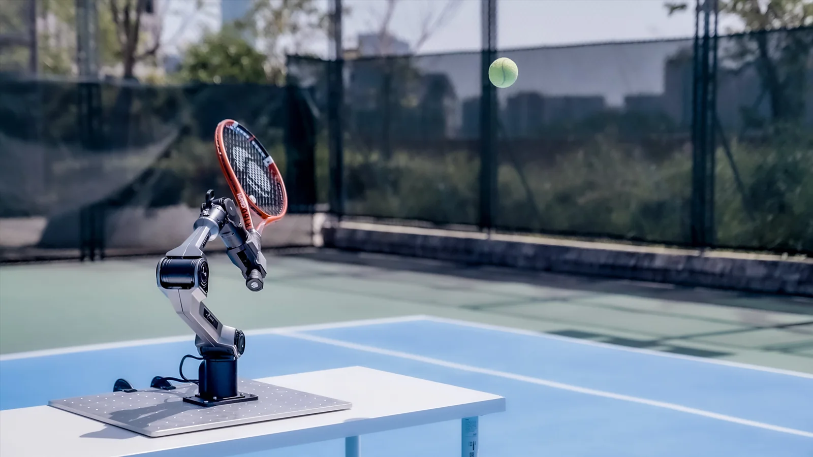 PiPER-Arm mit Tennisschläger auf einem Tennisplatz im Moment des Ballschlags (Herstellerfoto)